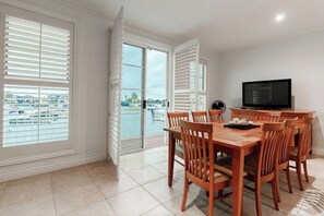 A dining area with a wooden table and chairs, a television, and a view of a marina through large windows.