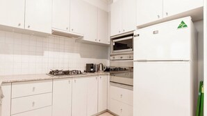 A kitchen with white cabinets, a gas stove, an oven, and a refrigerator.