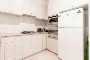 A kitchen with white cabinets, a gas stove, an oven, and a refrigerator.
