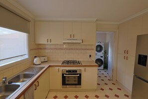 Eine kompakte Küche mit Spüle, Herd, Backofen und einer Waschmaschine im angrenzenden Raum.