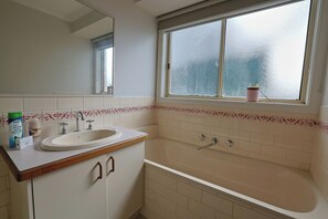 Een badkamer met een wastafel, spiegel, raam en bad.