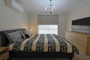 Een slaapkamer met een bed, een televisie, een dressoir, een kroonluchter en een raam.