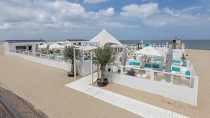 Rannalla sijaitseva lomakeskus, jossa on valkoisia rakennuksia, mukaan lukien teltta, jonka kyltissä lukee ”tiki beach”, ja rakennus, jossa on kalteva katto.