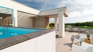 A modern outdoor pool area with a clear blue pool, a sun lounger, and a covered seating area with a view of the surrounding landscape. - Nice apartment for 4 people with WIFI, pool, A/C, TV, terrace and pets allowed (San Michele Al Tagliamento)