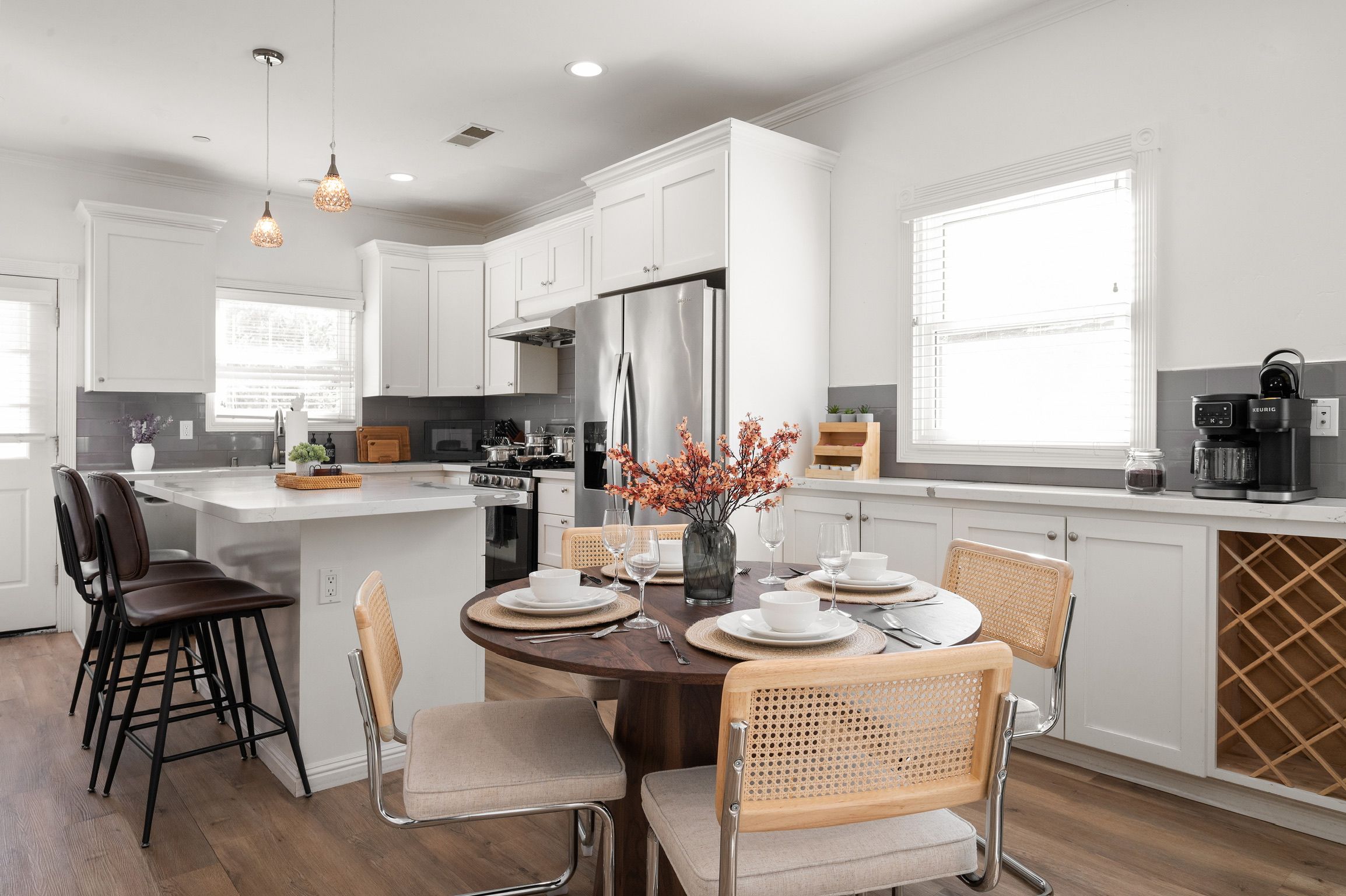 Una cocina moderna con armarios blancos, un refrigerador de acero inoxidable y un comedor con una mesa redonda para cuatro.