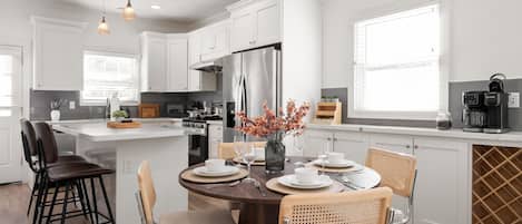 Una cocina moderna con armarios blancos, un refrigerador de acero inoxidable y un comedor con una mesa redonda para cuatro.