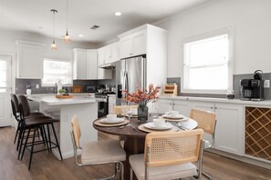 A modern kitchen with white cabinetry, a stainless steel refrigerator, and a dining area with a round table set for four. - Bright and Modern 3BR/2.5BA Home Near Downtown SJ, Airport, Stadiums & Tech Hubs (San Jose)