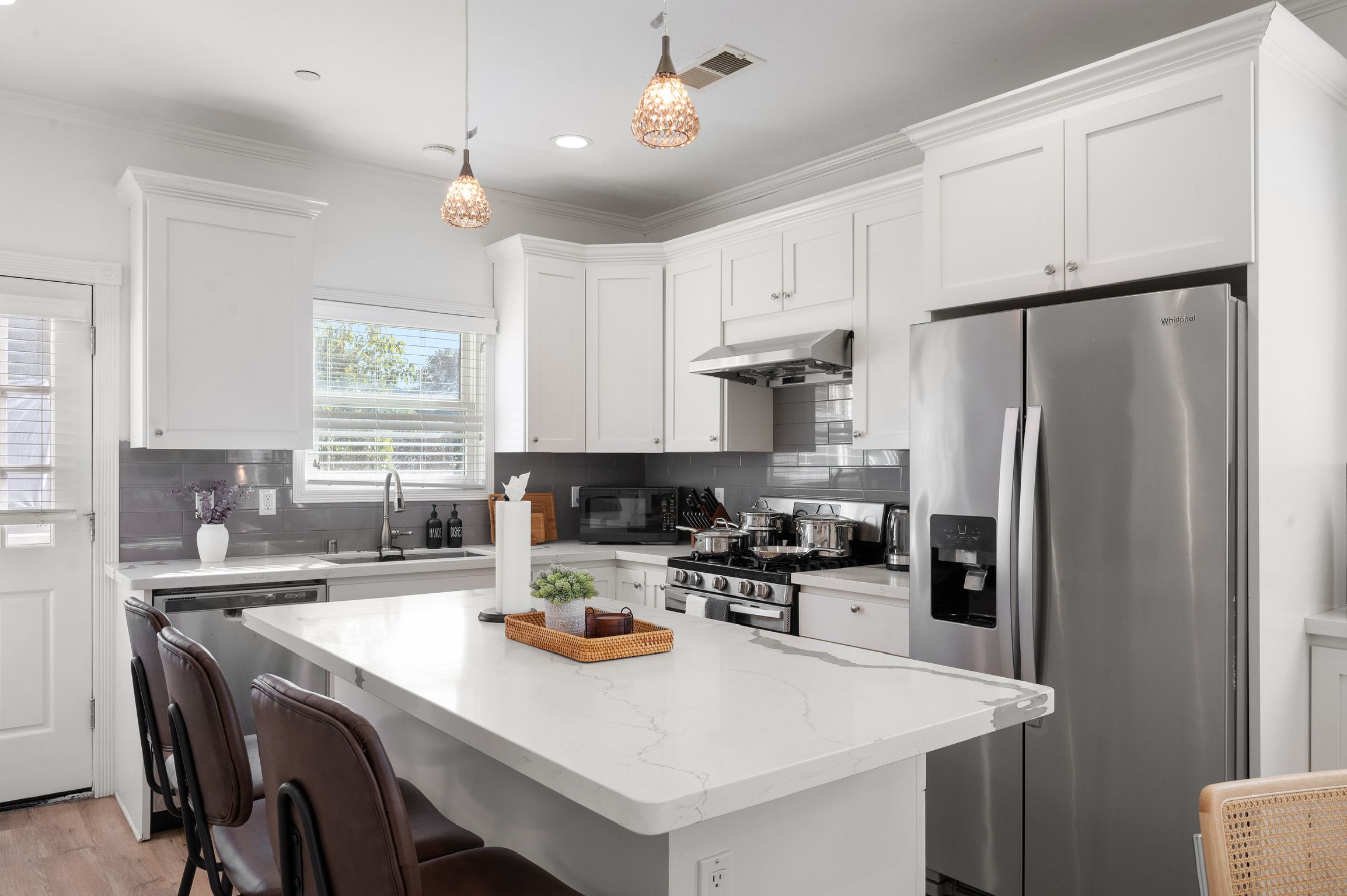 Une cuisine moderne avec des meubles blancs, un réfrigérateur en acier inoxydable, une cuisinière à gaz et des luminaires suspendus.