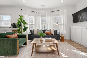 Ein modernes Wohnzimmer mit einem grünen Sessel, einem dunkelgrauen Sofa, einem Holztisch und einer großen Pflanze.