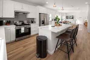 Una cocina moderna con armarios blancos, electrodomésticos de acero inoxidable y una isla central con taburetes de bar.