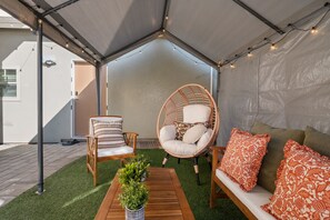 Un área de estar al aire libre con carpas, una mesa de madera, dos sillas y un sofá con cojines estampados.