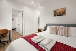 Habitación de hotel con cama, escritorio, silla, mesita de noche y un cuadro en la pared.
