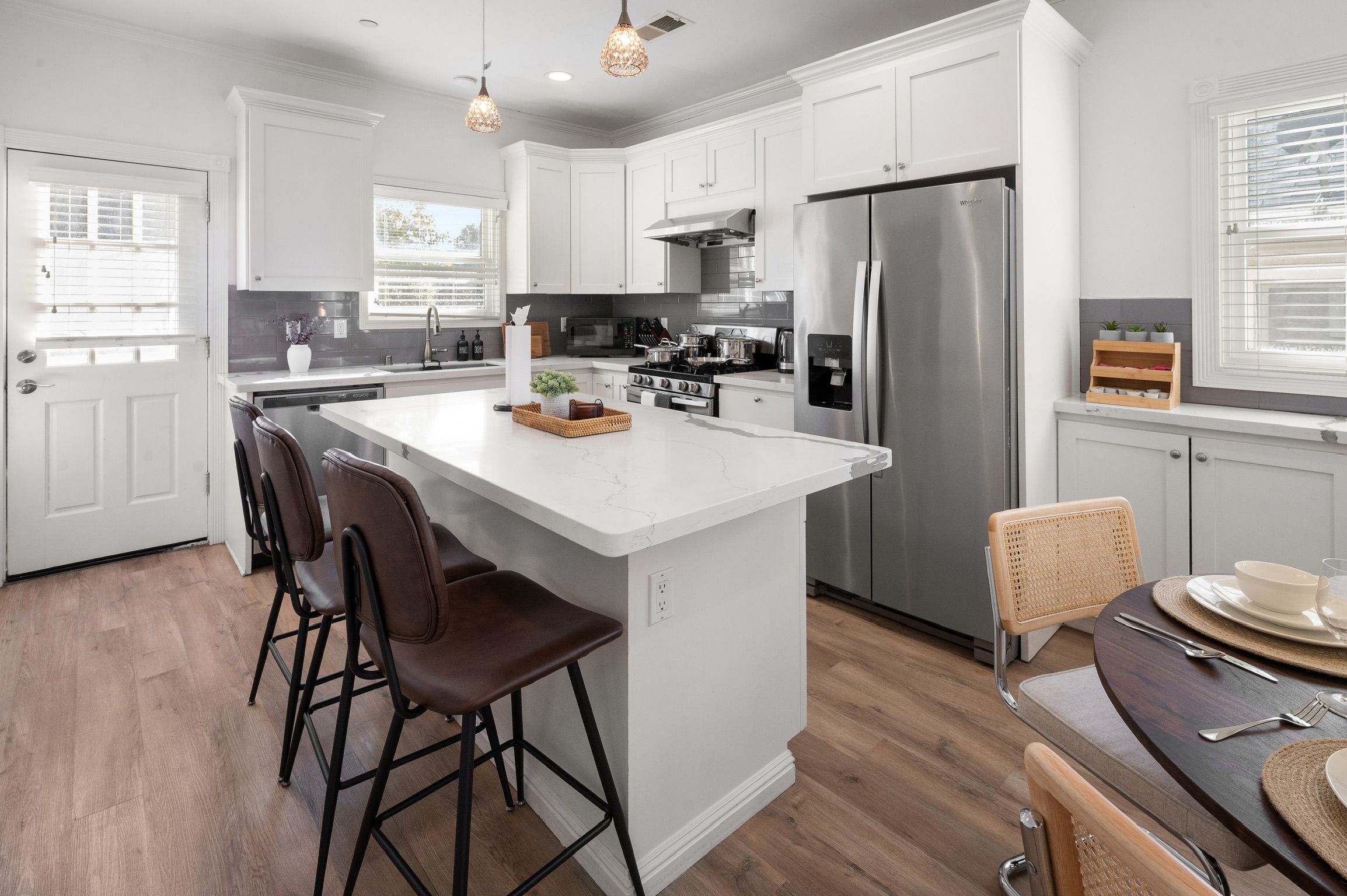 Een moderne keuken met witte kastjes, een centraal eiland, roestvrijstalen apparatuur, en een eetgedeelte met een donker houten tafel en stoelen.