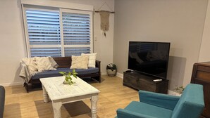 Een woonkamer met een bank, een salontafel, een televisie en een blauwe fauteuil.