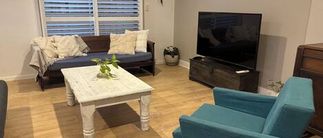 Un salon avec un canapé, une table basse, un téléviseur et un fauteuil bleu.
