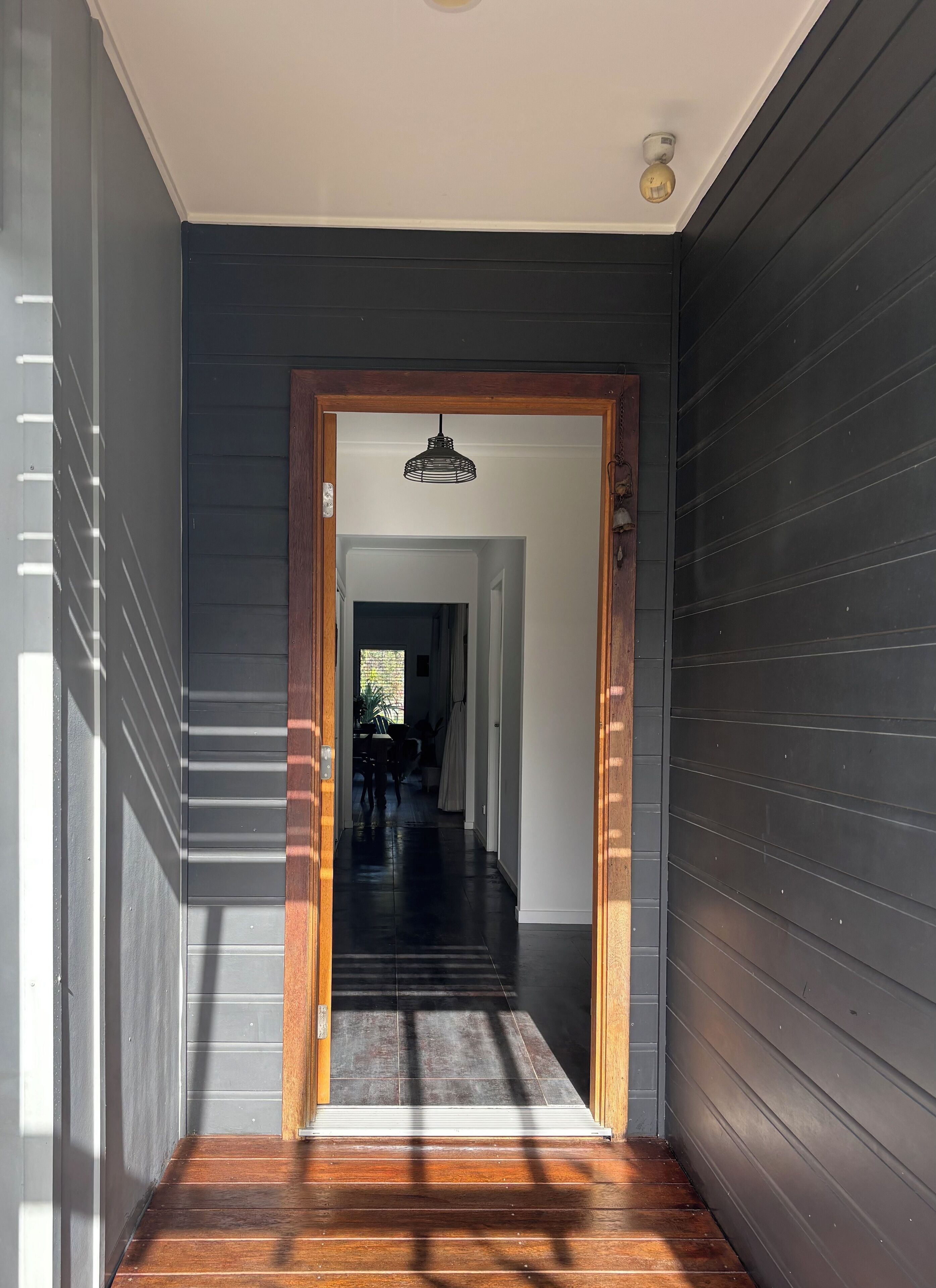 A hallway with dark siding walls, a wooden door frame, and a ceiling light fixture.