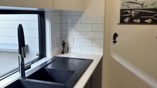 Een moderne keuken met een zwarte spoelbak, witte tegels en een illustratie van een vis aan de muur.