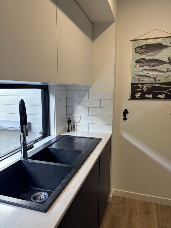 Una cocina moderna con un lavamanos negro, azulejos blancos e ilustración de un pez en la pared.