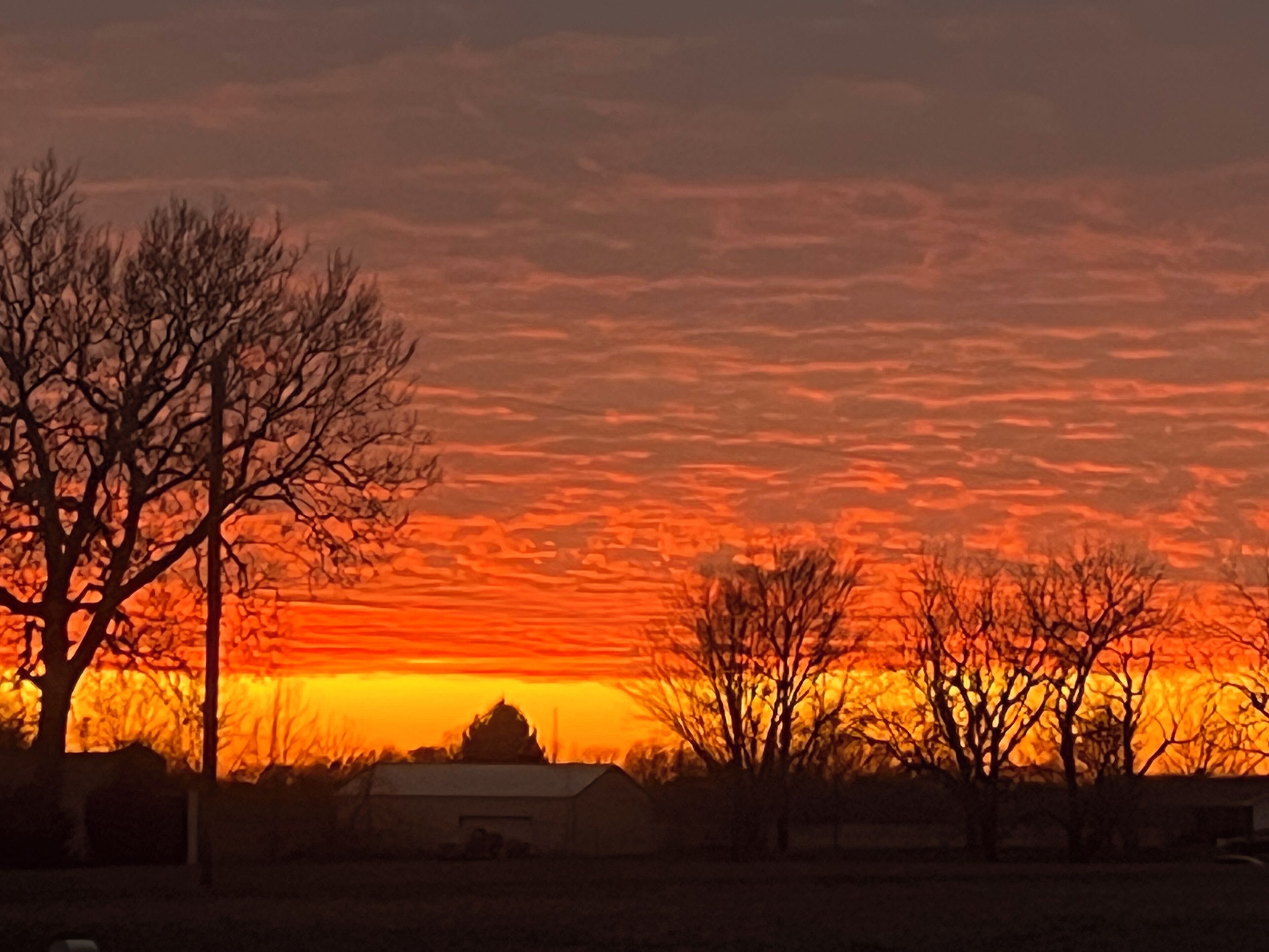 A sunset over a rural landscape with bare trees and a barn.