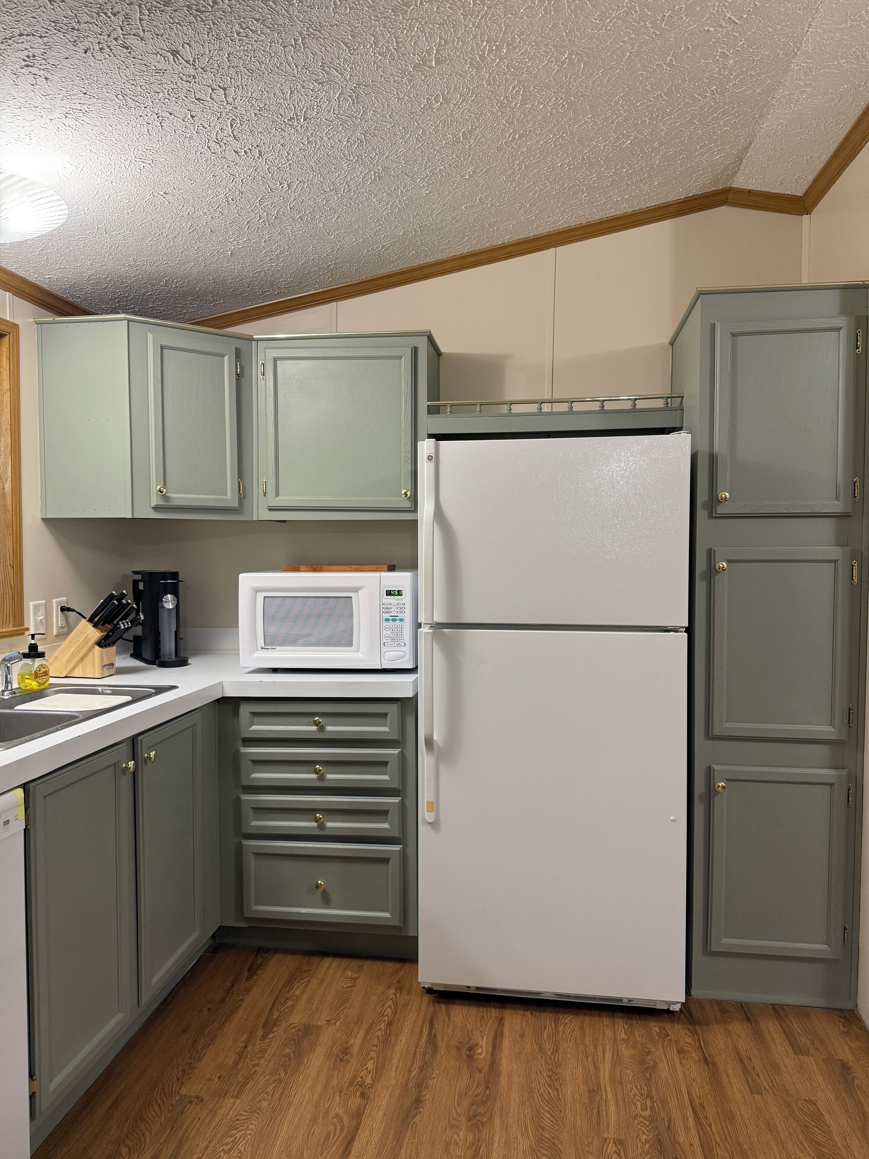 A compact kitchen with light green cabinets, a white refrigerator, a microwave, and a coffee maker.