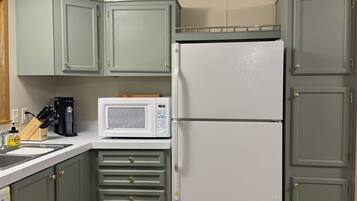 A compact kitchen with light green cabinets, a white refrigerator, a microwave, and a coffee maker.