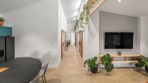 Een moderne kantoorruimte met een lange gang, een eetgedeelte met een tafel en stoelen, en een aan de muur bevestigde televisie.