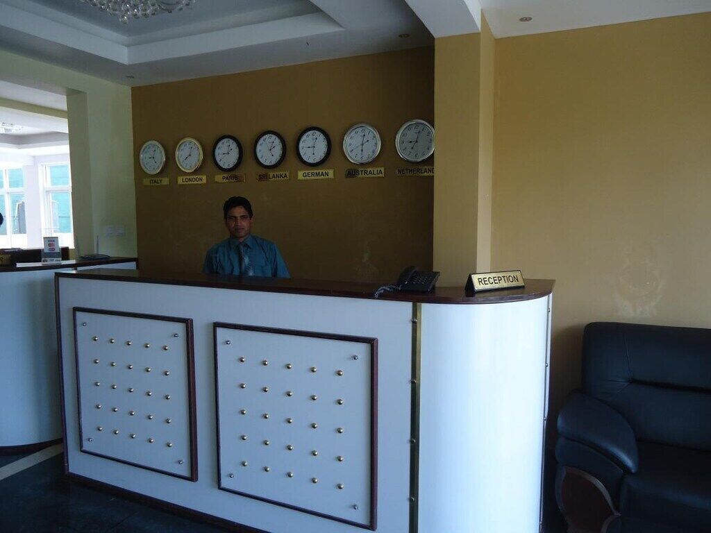 Una mesa de recepción con relojes mostrando la hora de varios países, un cartel de recepción y una zona de estar.