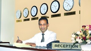 Vastaanottotiski, jossa on kelloja, ja jokaisessa kellossa on lappu, jossa on sen alueen nimi, esimerkiksi Italia, Lontoo, Pariisi, Saksa ja Australia.