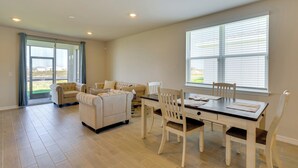 Ein geräumiges Wohnzimmer mit Essbereich, großen Fenstern und einer Glastür zum Patio.