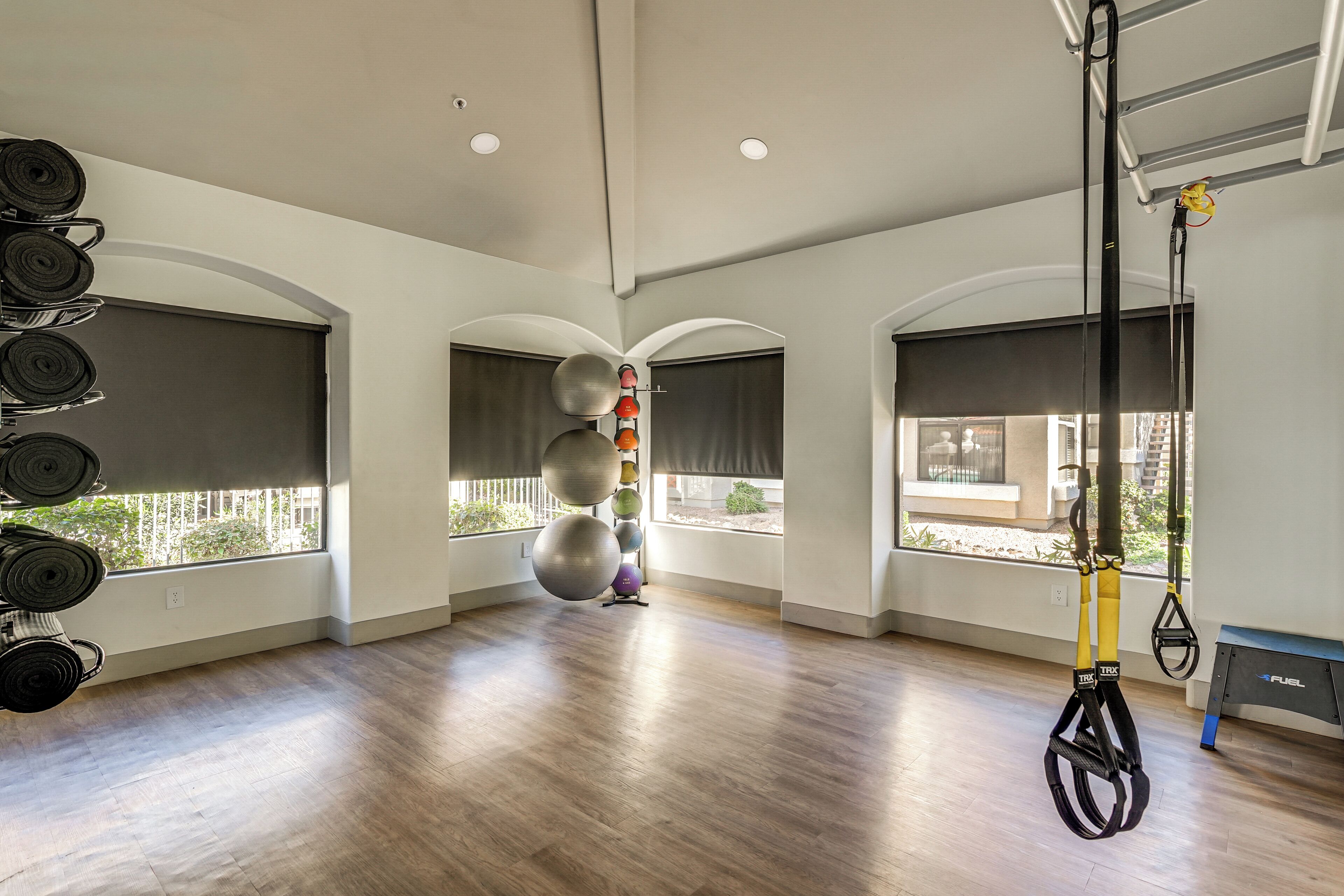 A spacious room with wooden flooring, large windows, and exercise equipment including a TRX suspension trainer.