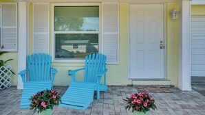 Eine Veranda mit zwei blauen Adirondack-Stühlen, einer Fußmatte und zwei Blumentöpfen.