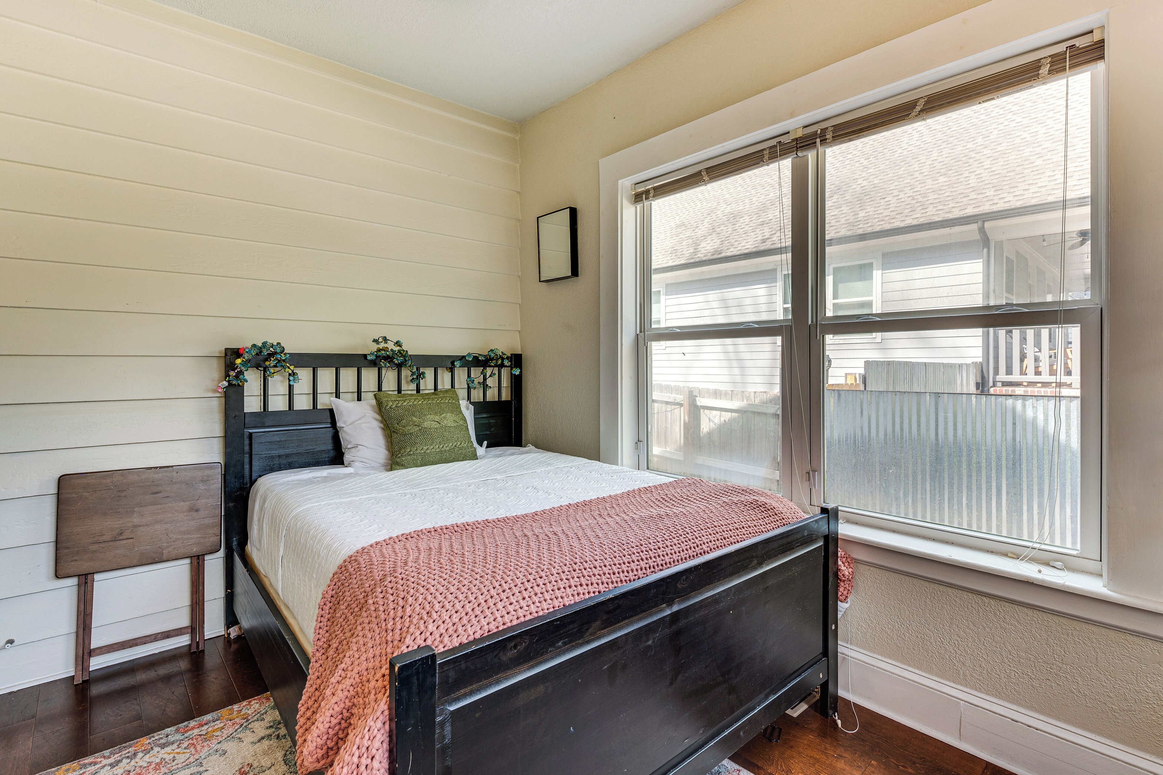 Une chambre à coucher avec un lit, une table de chevet, une fenêtre avec des stores et une vue sur une clôture.