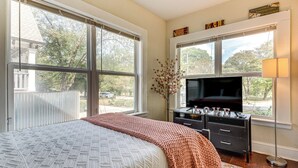 Ein Schlafzimmer mit einem großen Bett, einem Schminktisch, einem Fernseher und einem Fenster mit Blick nach draußen.