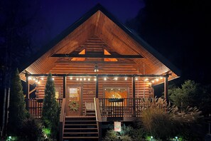 Una cabaña de troncos con fachada de madera, un porche con luces colgantes y una escalera que lleva a la entrada.