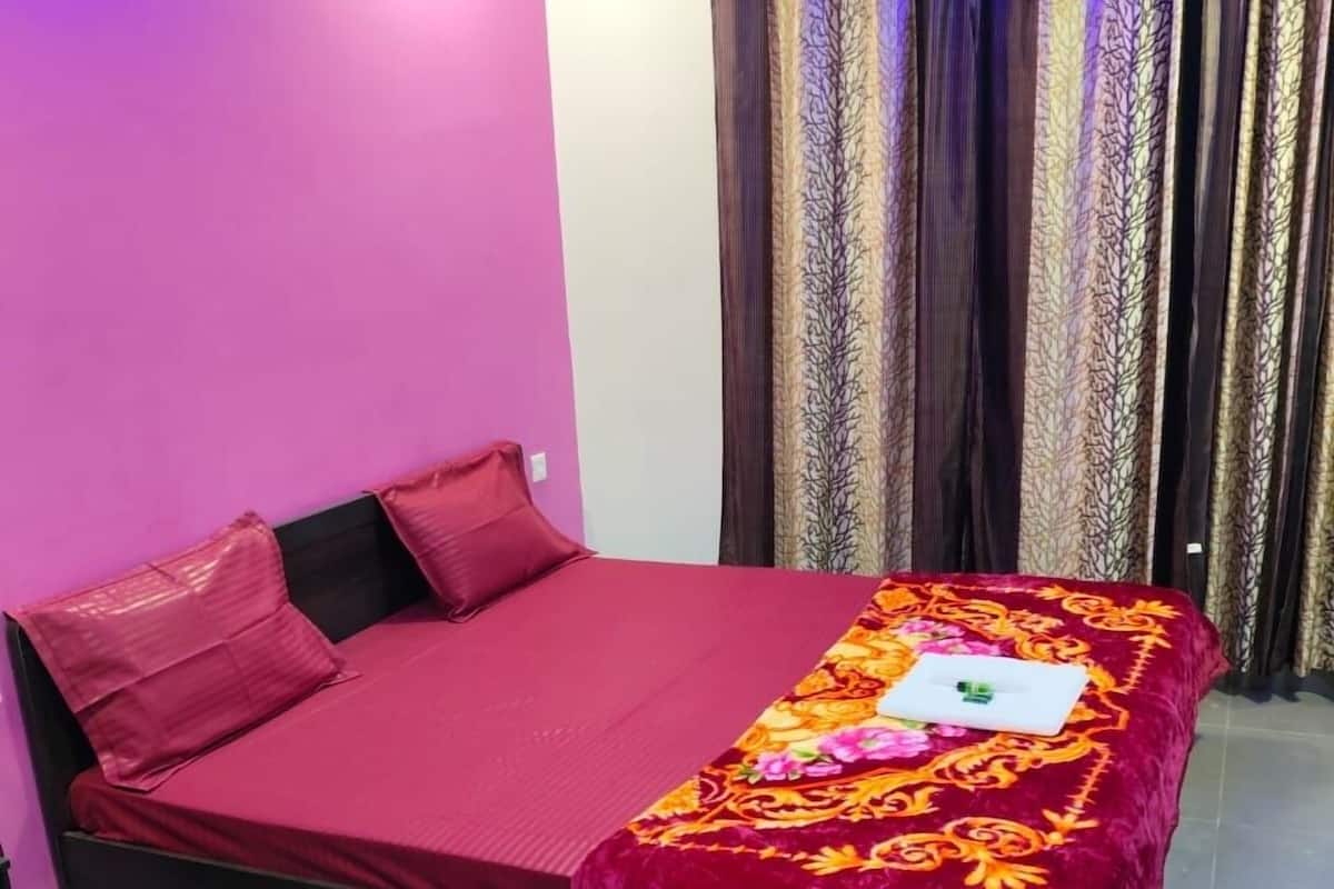 A bed with a red mattress and a decorative cover, a pink wall, and curtains with a leaf pattern.
