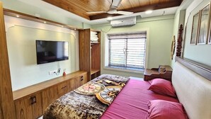 Un dormitorio con cama, televisión montada en la pared, ventana con persianas y ventilador de techo.