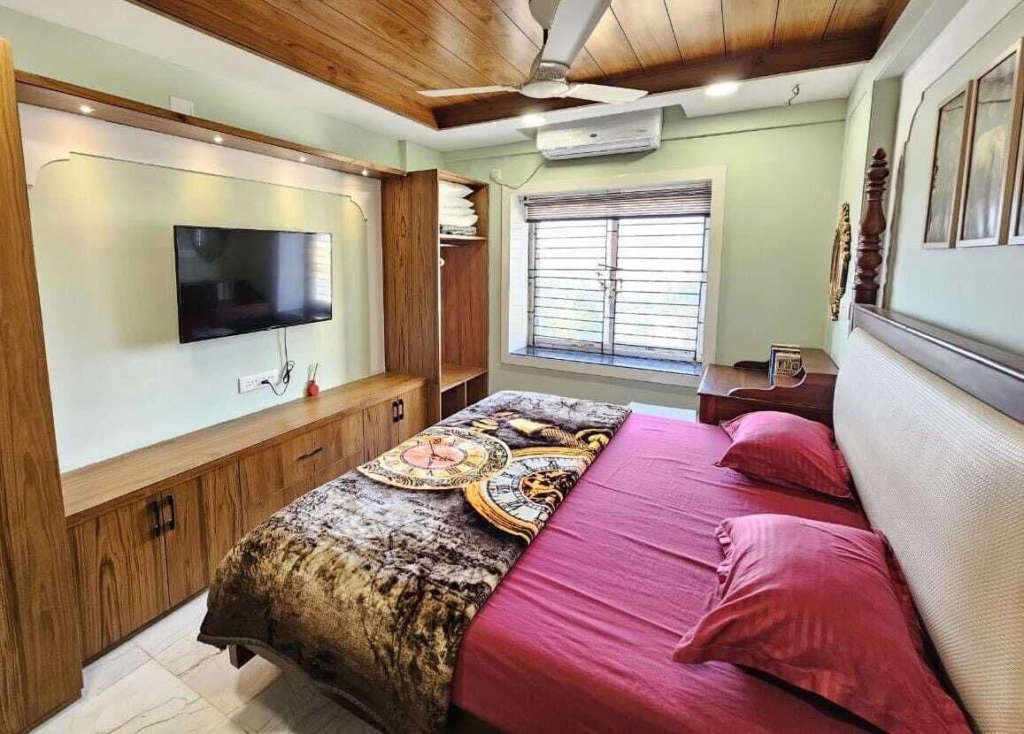 Une chambre à coucher comprenant un lit, un téléviseur, une fenêtre avec des stores et un ventilateur de plafond.