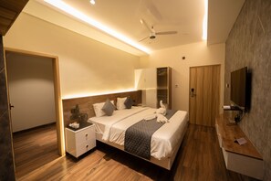 A modern hotel room with a wooden floor, a bed with a quilted blanket, a nightstand, a desk, a mirror, and a ceiling fan. - Sivashree Residency (Tiruvannamalai)