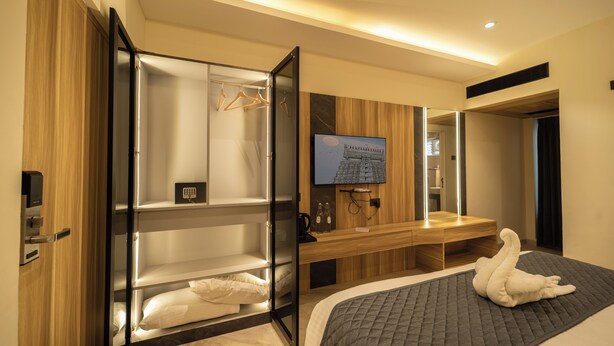 Habitación de hotel con cama, armario empotrado, tocador con espejo y televisor en la pared.