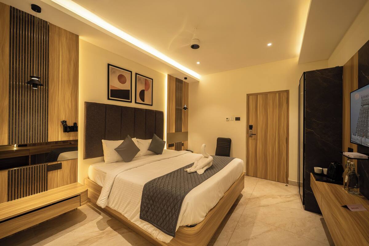 Een moderne hotelkamer met een groot bed, houten lambrisering, een flatscreen televisie en een bureau met een fles en glazen.