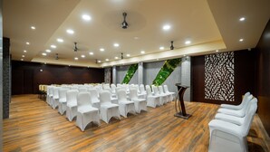 Un salón de conferencias con hileras de sillas blancas, un atril y suelo de madera.