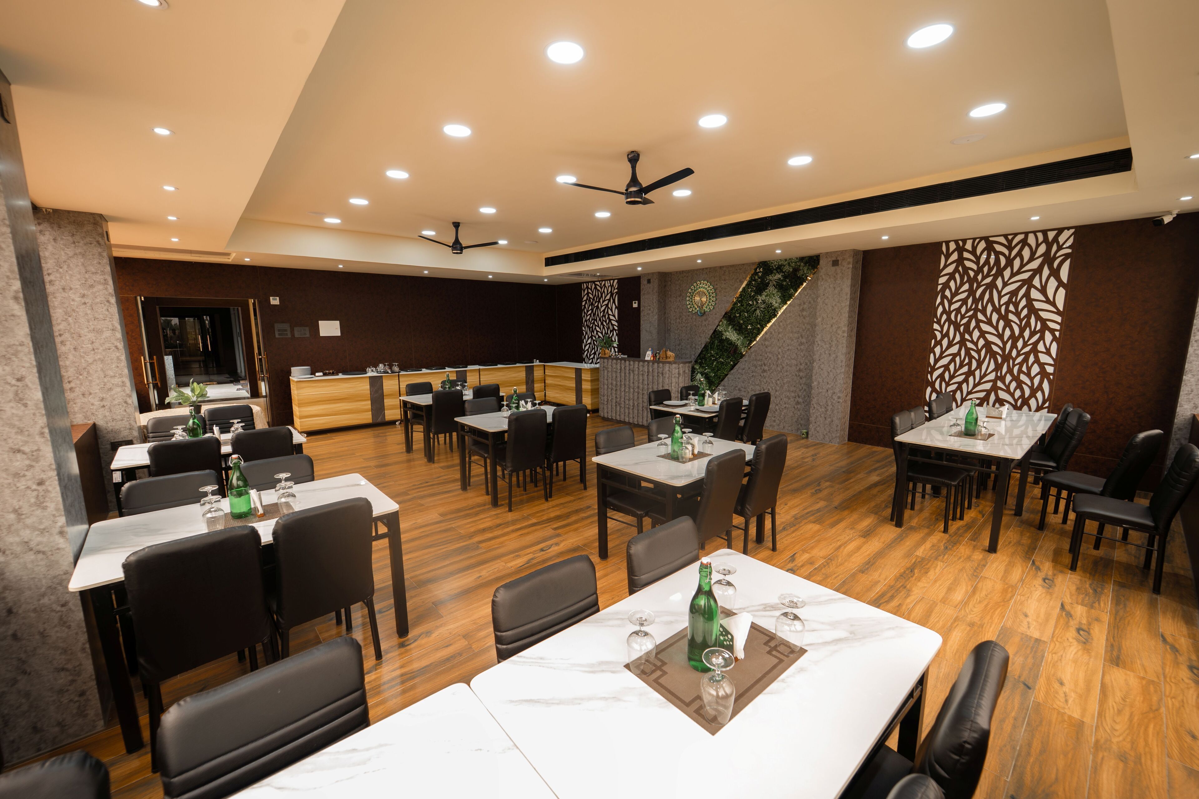 Een ruim restaurant met meerdere tafels en stoelen, plafondventilatoren en een decoratieve wand.