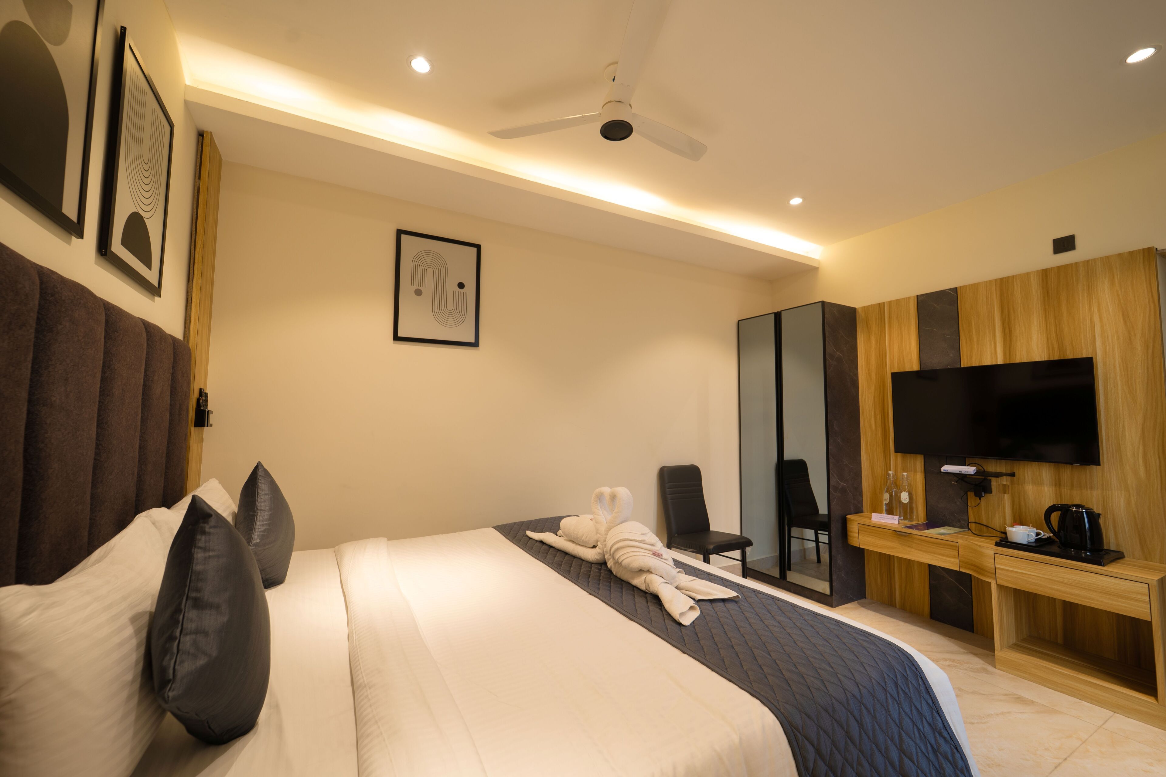 A hotel room with a bed, a desk, a chair, a television, and artwork on the walls.