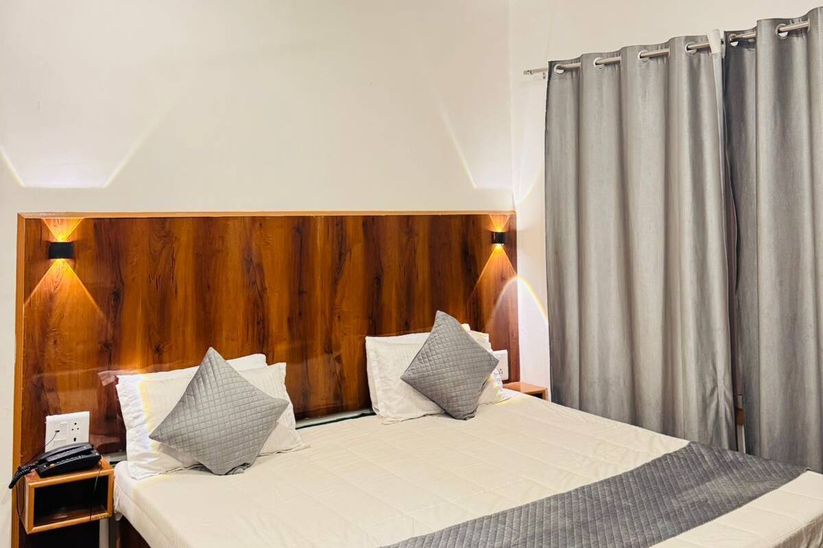 A hotel room with a wooden headboard, a bed with white and gray bedding, a nightstand with a phone, and a ceiling fan.