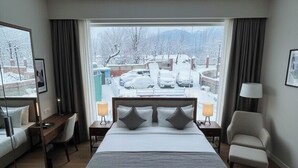 A hotel room with a large bed, a desk, a chair, and a view of a snowy landscape. - The Gulmarg Palace (Gulmarg)