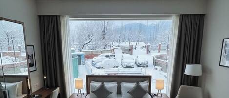 A hotel room with a large bed, a desk, a chair, and a view of a snowy landscape.