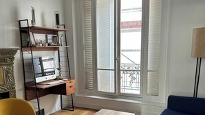 A living room with a wooden floor, a blue sofa, a yellow armchair, a wooden coffee table, a bookshelf, and a window with shutters. - Cosy Paris apartment 5 minutes from Bastille! Ideal for sightseeing! (Paris)