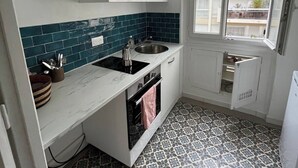 A compact kitchen with white cabinets, a black stove, and a window with a view of a building. - Cosy Paris apartment 5 minutes from Bastille! Ideal for sightseeing! (Paris)