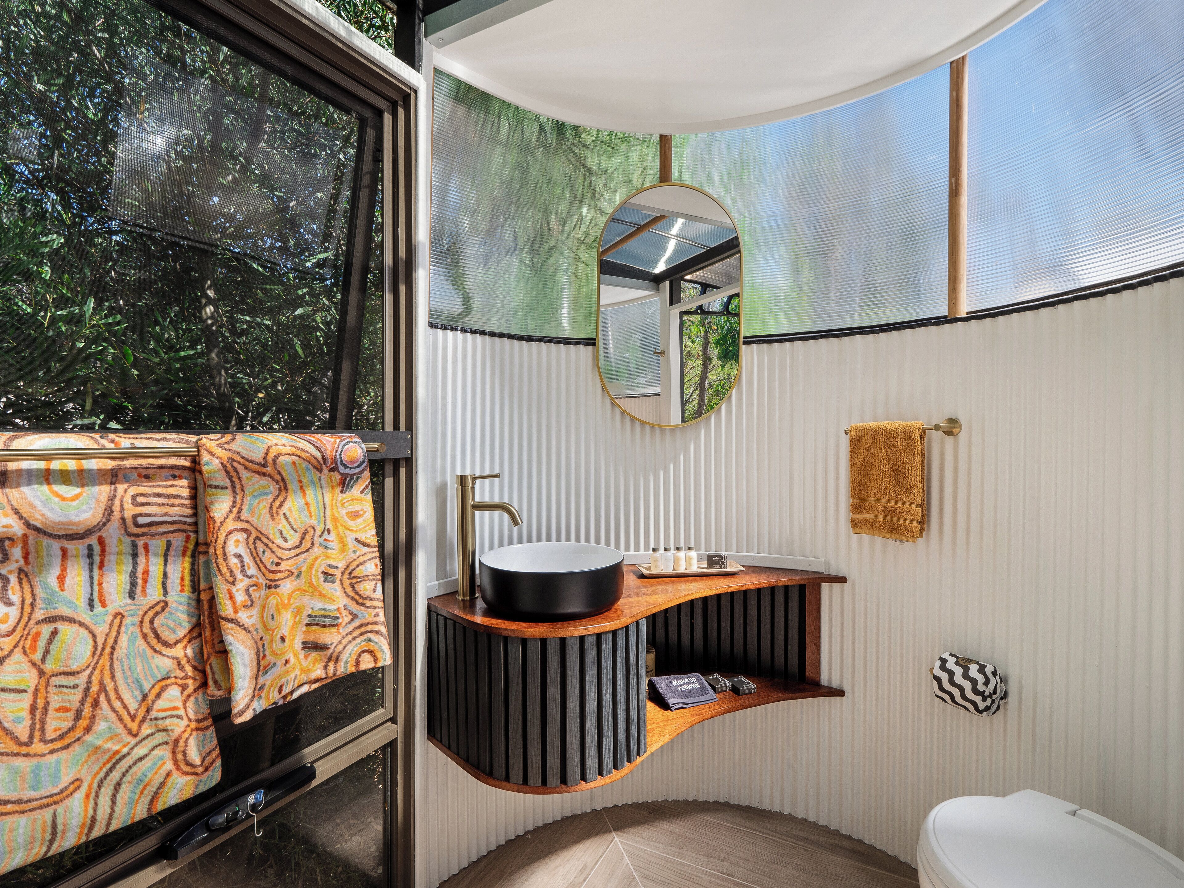 A bathroom with a modern design, featuring a curved vanity, a round mirror, and a toilet.