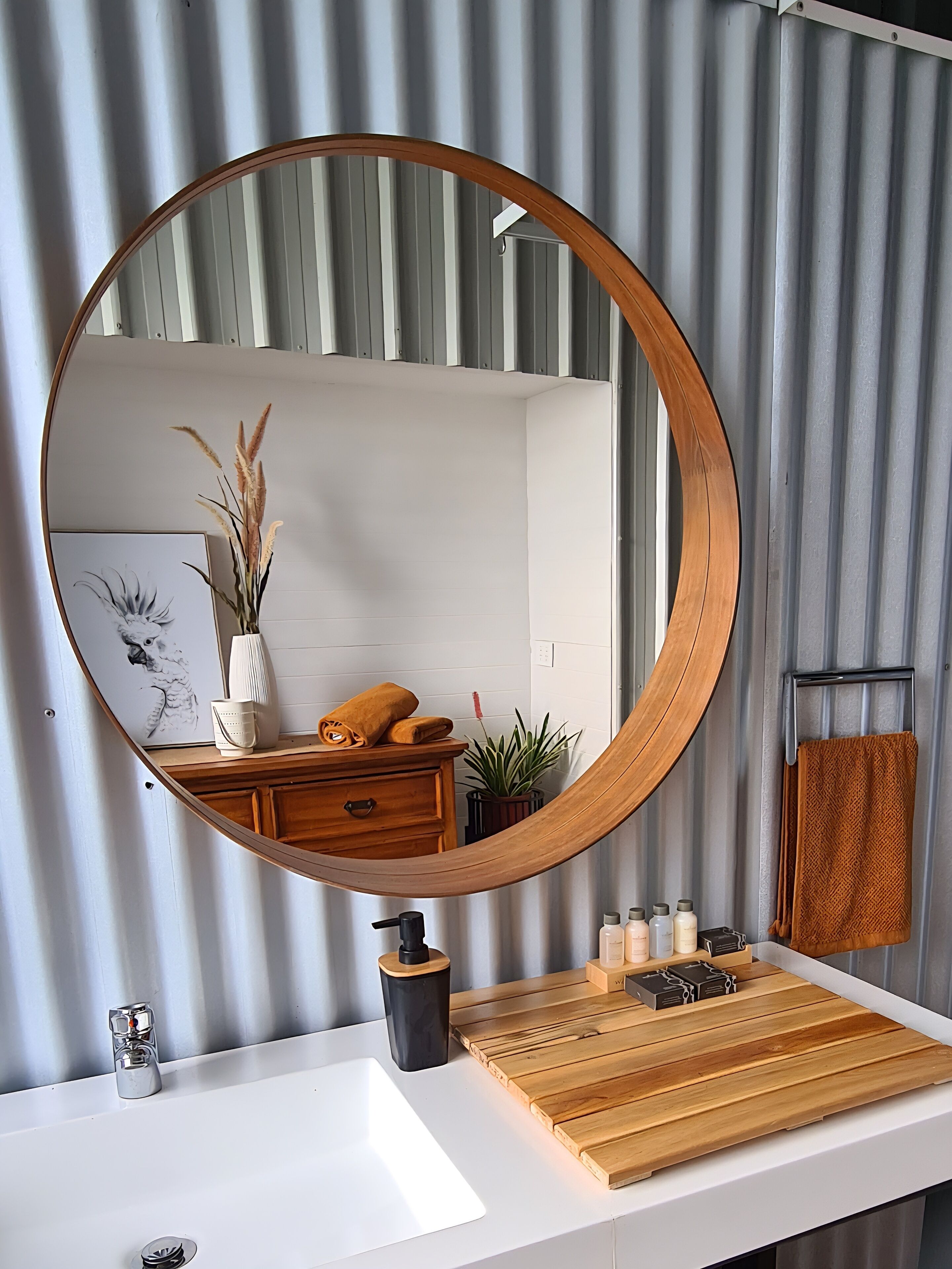 A bathroom with a round mirror, wooden vanity, white sink, and a towel rack.